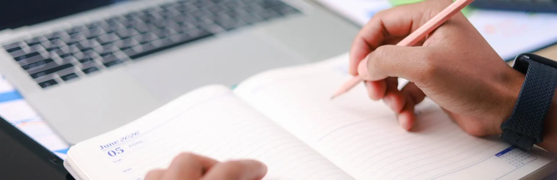 Business professional writing notes in planner beside laptop and charts. Concept of productivity, scheduling, planning, strategy, and office workflow.